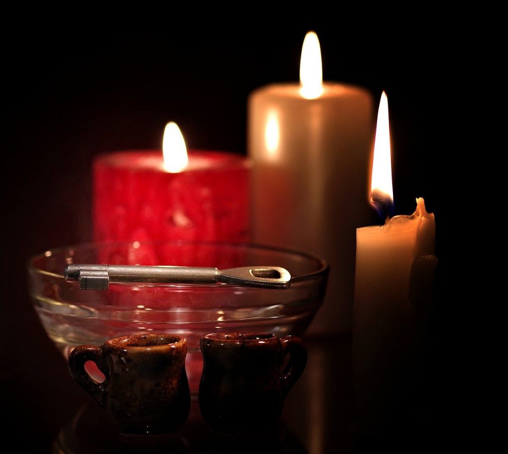 Ilustracja andrzejek - w tle trzy kolorowe palące się świece, przed nimi szklana misa, na której leży klucz, przed misą dwa małe gliniane kubeczki.